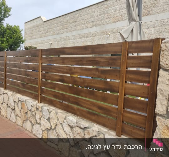 גדר עץ חומה על קיר אבן בגינה